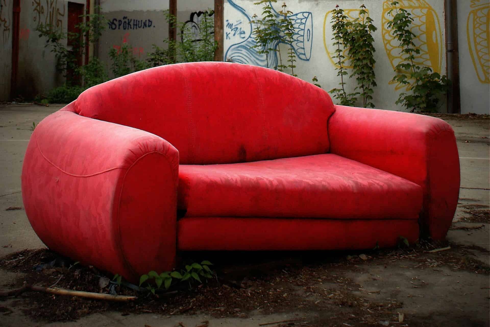 A vibrant red couch placed in a lush green field under a clear blue sky.