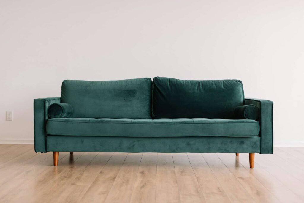 A green couch positioned on a polished hardwood floor, creating a cozy and inviting living space.