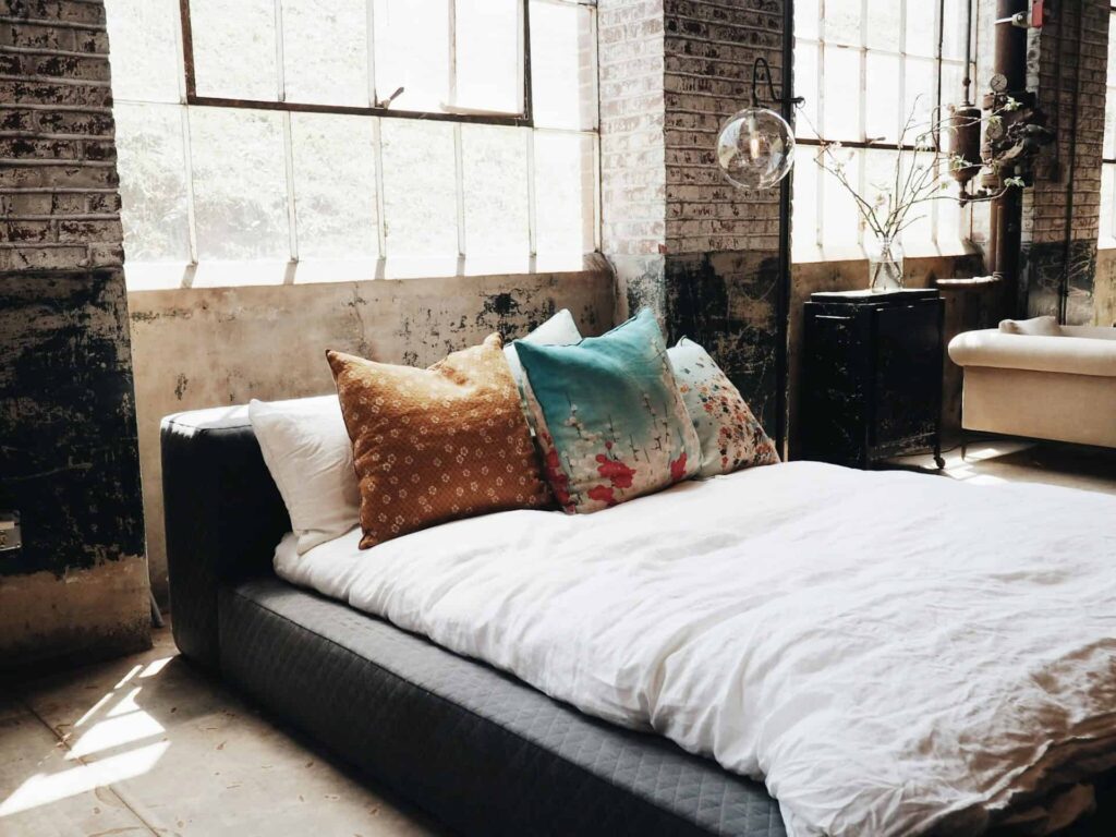 A bed adorned with pillows beside a window, showcasing an industrial decor style in a stylish room setting.